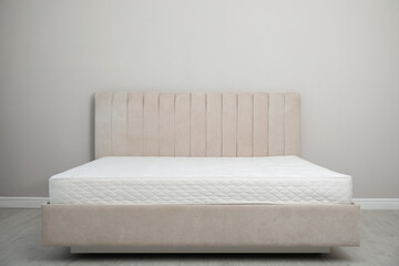Comfortable bed with modern orthopedic mattress near grey wall indoors
