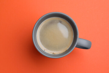 Grey mug of freshly brewed hot coffee on orange background, top view