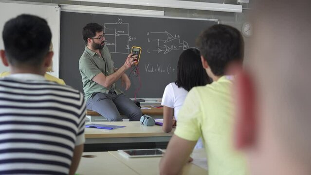 High School Teacher explaining electrical voltage tester device To Pupils learning In Technology Electronics course