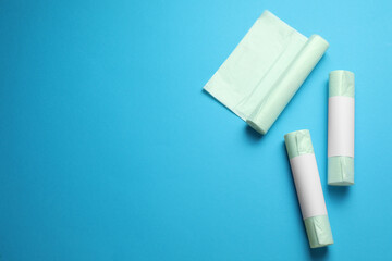 Rolls of different garbage bags on light blue background, flat lay. Space for text