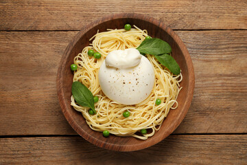 Bowl of delicious pasta with burrata, peas and spinach on wooden table, top view