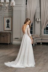 The beautiful woman posing in a wedding dress. Young beautiful happy bride wearing white wedding dress and posing in bright empty interior. Wedding fashion. Expensive Lace bust.