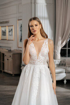 The beautiful woman posing in a wedding dress. Young beautiful happy bride wearing white wedding dress and posing in bright empty interior. Wedding fashion. Expensive Lace bust.