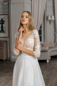 The beautiful woman posing in a wedding dress. Young beautiful happy bride wearing white wedding dress and posing in bright empty interior. Wedding fashion. Expensive Lace bust.