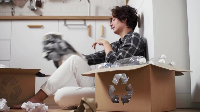 Middle-aged woman removes things from her head. Tired woman engaged in processing things. Unnecessary items sorted in recycling box. Woman is holding donation box. Cardboard boxes for recycling
