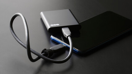 Black external portable SSD connected to a smartphone on a dark gradient background. Portable Solid State Drive. OTG interface. Concept of modern technology and the use of SSD disk.