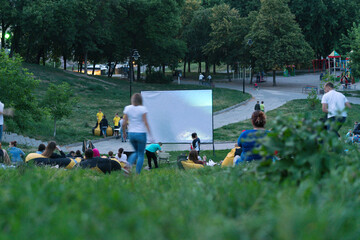 Many people watch movies in open-air cinema in the green park. Empty blank. Comfortable. Dusk. Enjoy. Friends. Illuminated. Pillow. Blanket. Projector. Nightlife. Public. Watch. Relaxing. Relaxation