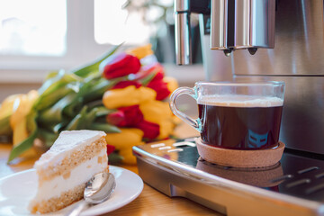 Cup of coffee with milk, piece of cake and tulips flowers on wooden kitchen table. Freshly brewed...
