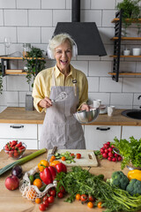 Senior attractive woman listening to music and singing in her headphones in the kitchen. Active lifestyle of mature people, enjoying life, having fun. Using whisk as microphone while cooking food