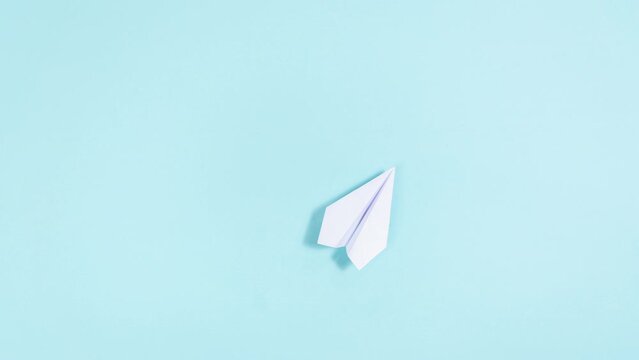 4k White paper airplane takes off, describing a circle and flies through the clouds, then lands. Blue background. Travel and transportation concept. Stop motion animation. Copy space.