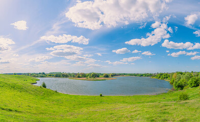A beautiful lake in the middle of green hills under a blue sky with clouds in the village of Vchorayshe, Zhytomyr Region, Ukraine