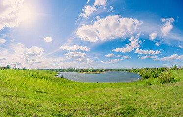 Fototapeta na wymiar Green field and blue pond in the village Vchorayshe, Zhytomyr Region, Ukraine