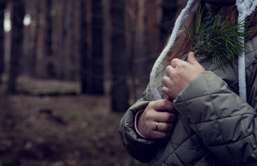 A girl in light clothes clutches a pine branch to her chest. The girl shows her love for nature and the forest.