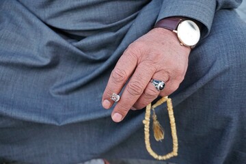 Arabischer alter Mann in grauem traditionellem Gewand mit Zigarette und goldgelber Kette in Hand 