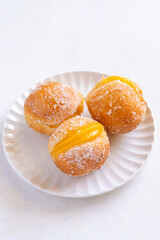Bola de Berlim, or Berlin Ball, a Portuguese pastry made from a fried doughnut filled with sweet eggy cream on a white plate
