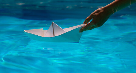 Paper boat with hand. Paper boat sailing on blue water surface. Origami paper boat.