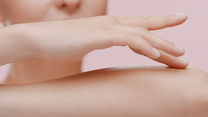 Good-looking young slim Caucasian woman strokes her forearm on pale pink background | Unwanted arm hair removal concept