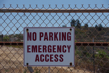 Sign on a fence at an industrial facility NO PARKING EMERGENCY ACCESS