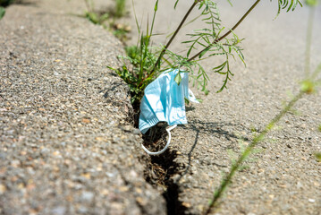 Used medical mask and plants in a crack on the pavement. ecological concept about the impact of the pandemic on the increase in the amount of garbage