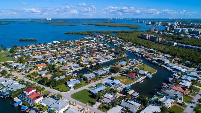 Aerial Drone View of Homes Featuring Canals on Blue Bay Waters Surrounded by Mangroves in Bonita Springs, Florida and the Gulf of Mexico in the Background with a Clear Sky
