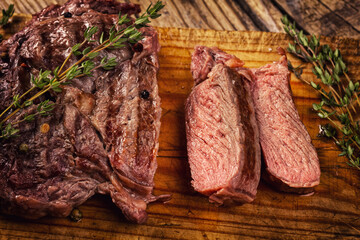 Juicy medium rare beef steak slices on wooden board with herbs spices and salt.