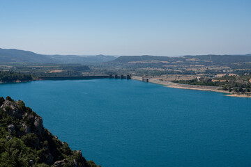 Fototapeta na wymiar Large blue reservoir and distant El Grado Dam, Hydro-Electricity Generation, Huesca, Spain, a concrete hydro-electric reservoir dam, clear blue sky