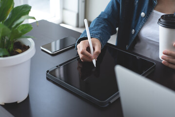 Closeup of young asian business woman in casual wear using stylus pen touching on digital tablet,...