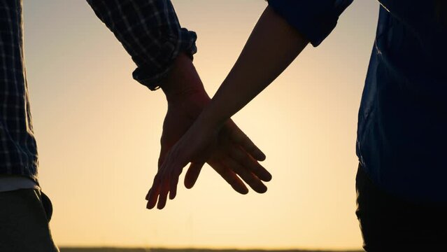 Loving couple holding hands against backdrop of sun. Close up of guy, girl meet holding hands together. Hands of man, woman touch hands outdoors. Happy family, husband, wife. Family in park at sunset