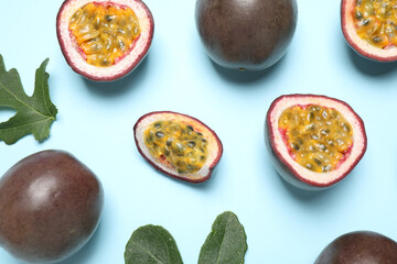 Fresh ripe passion fruits (maracuyas) with green leaves on light blue background, flat lay