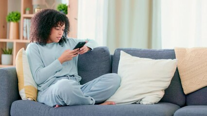 Relaxed woman texting on a phone while being lazy on her couch. Carefree young female smiling while chatting to her friends online, browsing the internet and scrolling social media on a device