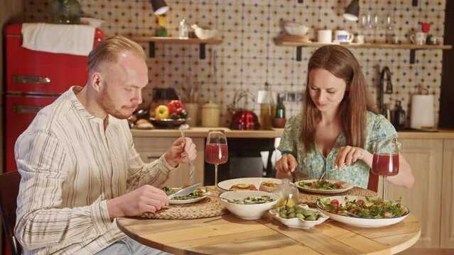 Couple having healthy dinner at home. Man and woman eating healthy vegetable salad and talking with each other while having dinner in vintage kitchen at home
