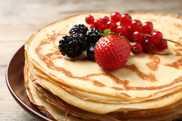 Delicious thin pancakes with berries on plate, closeup