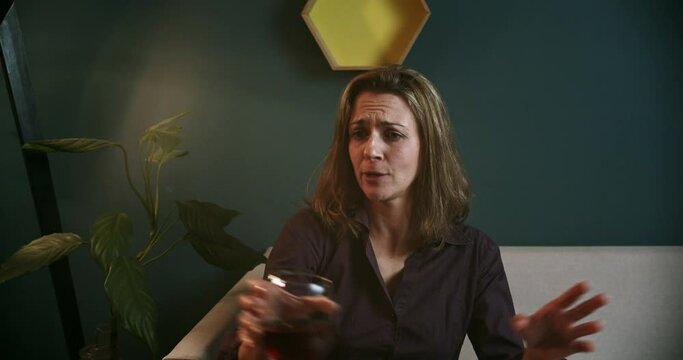 Woman on sofa smiling and talking to someone with a red wine glass. 4K