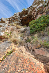 Obraz premium Mountain trails on Lions Head, Cape Town, South Africa. Rocky trail on a mountain with plants and grass against clear cloudy blue sky. Low angle of tourist attraction in remote location in nature