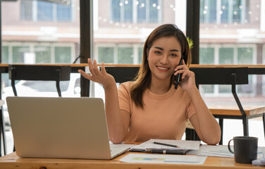 Smiling businesswoman talking on mobile phone and using laptop in office