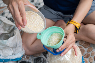 Woman fill rice grains into plastic bottle by a funnel. Funnel rice into a bottle until you're...
