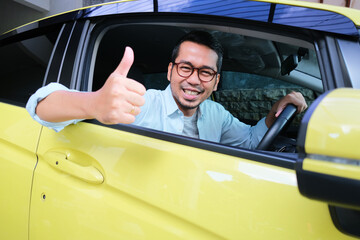 Adult Asian man smiling happy and give thumb up from inside car driver seat window
