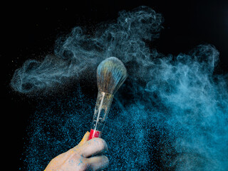 Woman shaking off blue powder from a brush on a black background. 