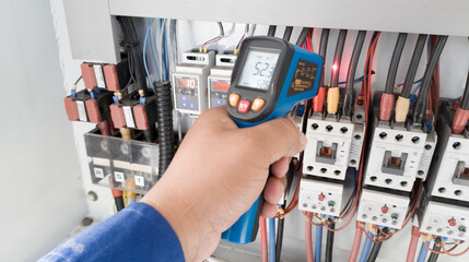 an electrician is using a thermogun to analyze sub-wires and components, use digital infrared thermometer to find out overcurrent loads, and abnormalities in the panel's electrical system.