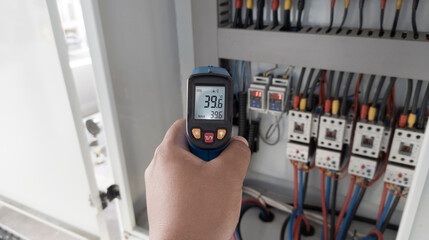 an electrician is using a thermogun to analyze sub-wires and components, use digital infrared...