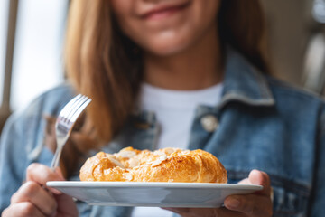 Closeup image of a young woman holding and eating a fresh almond croissant