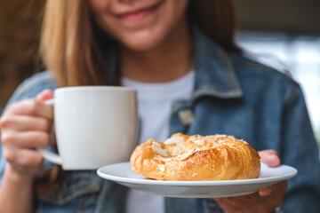 Closeup image of a young woman drinking coffee and eating a fresh almond croissant