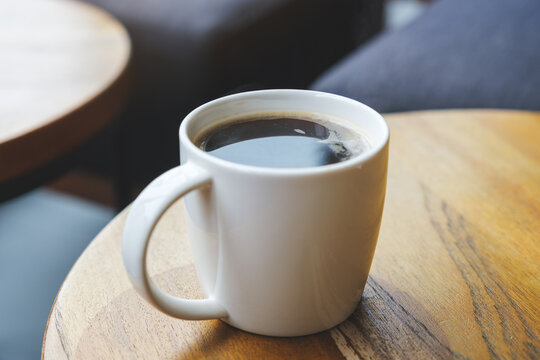Closeup image of a white cup of hot coffee on wooden table in cafe