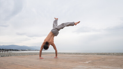 Obraz premium Shirtless caucasian man doing backflip on pebble beach. 