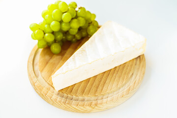 piece of brie cheese, white grapes on wooden round cutting board. Side view, close-up