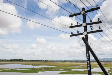 Electric pole beside railway In the middle of the meadow and the blue sky.