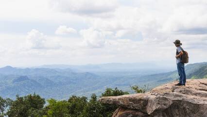 Naklejka premium Asian man travel and standing on the edge of the mountain with forest landscape background.Concept of travel in spring season at Thailand.