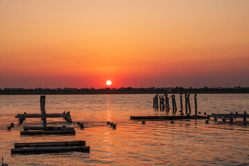 Beautiful red and orange sunset over the sea. The sun goes down over the sea. A flock of cormorants sits on a old sea pier in orange sunset light