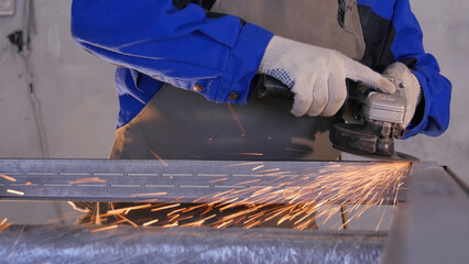 Craftsman sawing metal with disk grinder in workshop. Grinding metal with sparks flying. Electric...