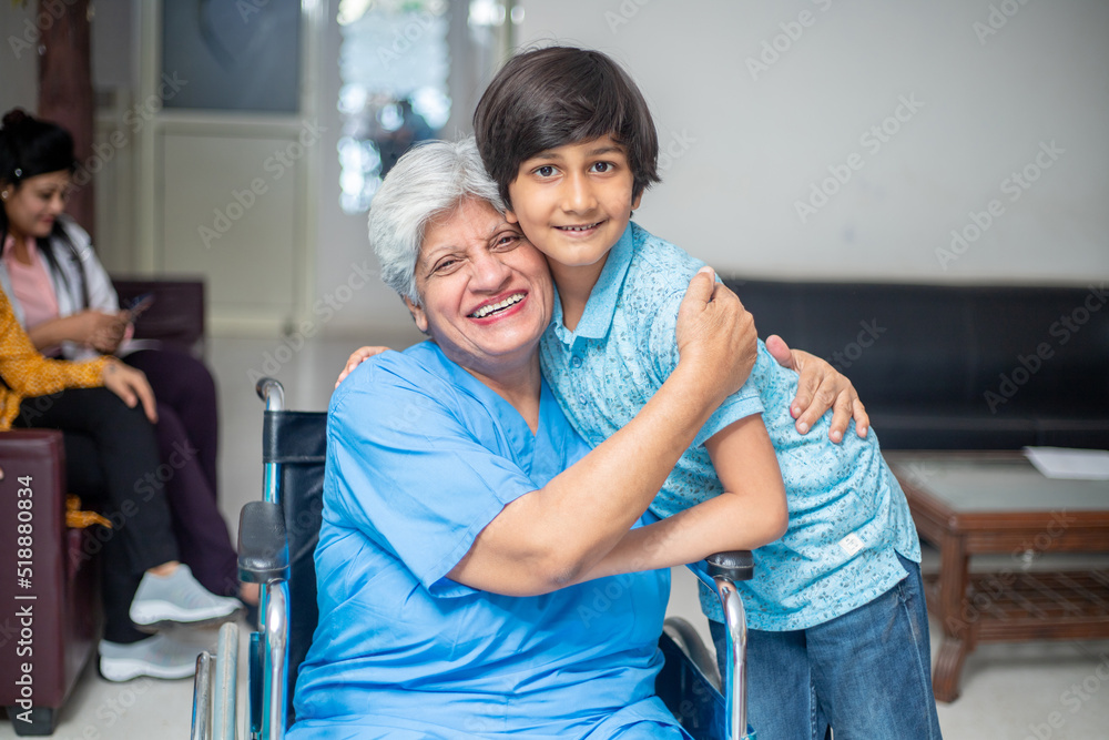 Wall mural Smiling indian senior woman granny sit in wheelchair hug her grandson at hospital. healthcare concept.